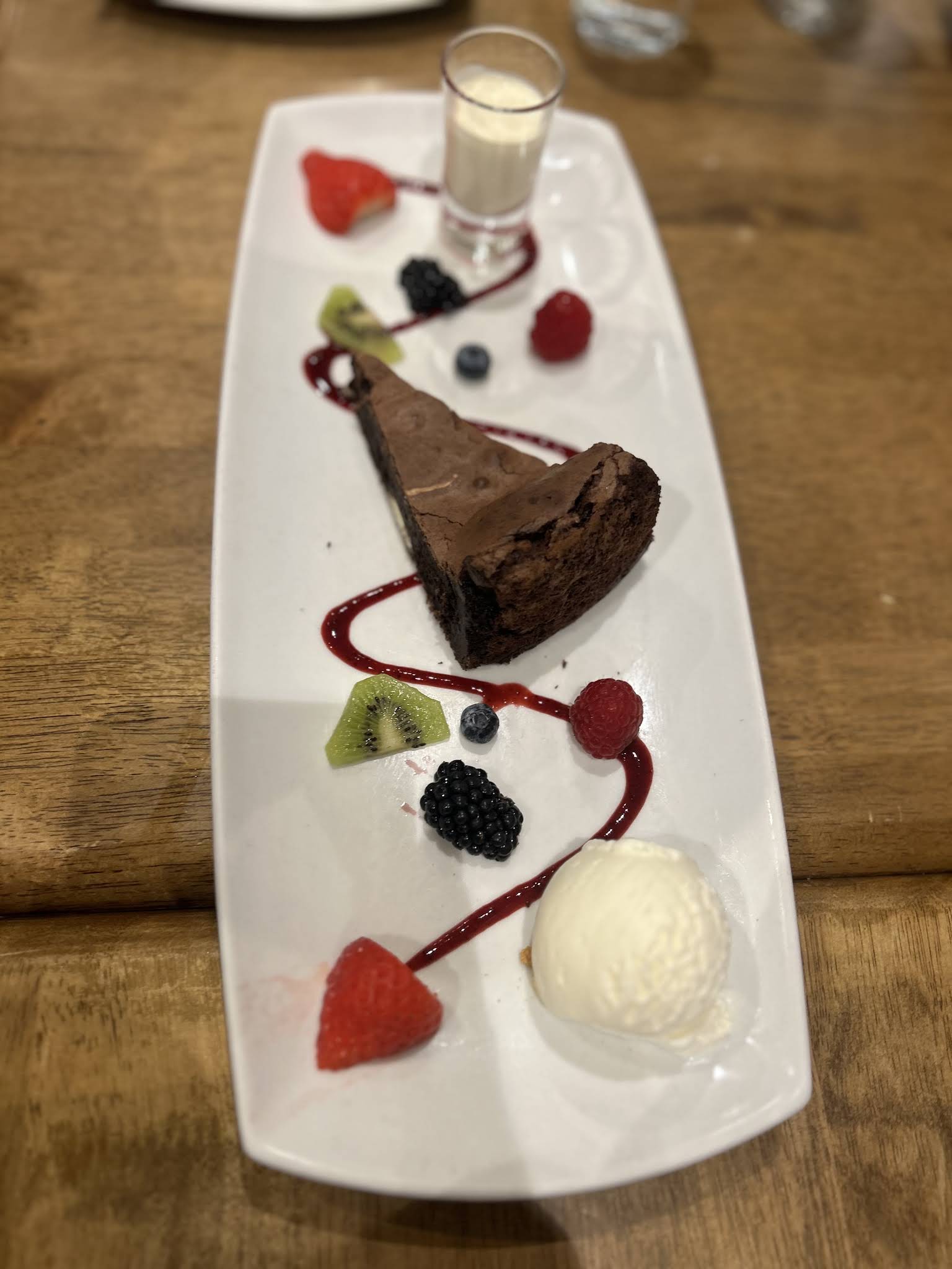 A complete white dessert platter with chocolate cake, fruit, ice cream and a small glass