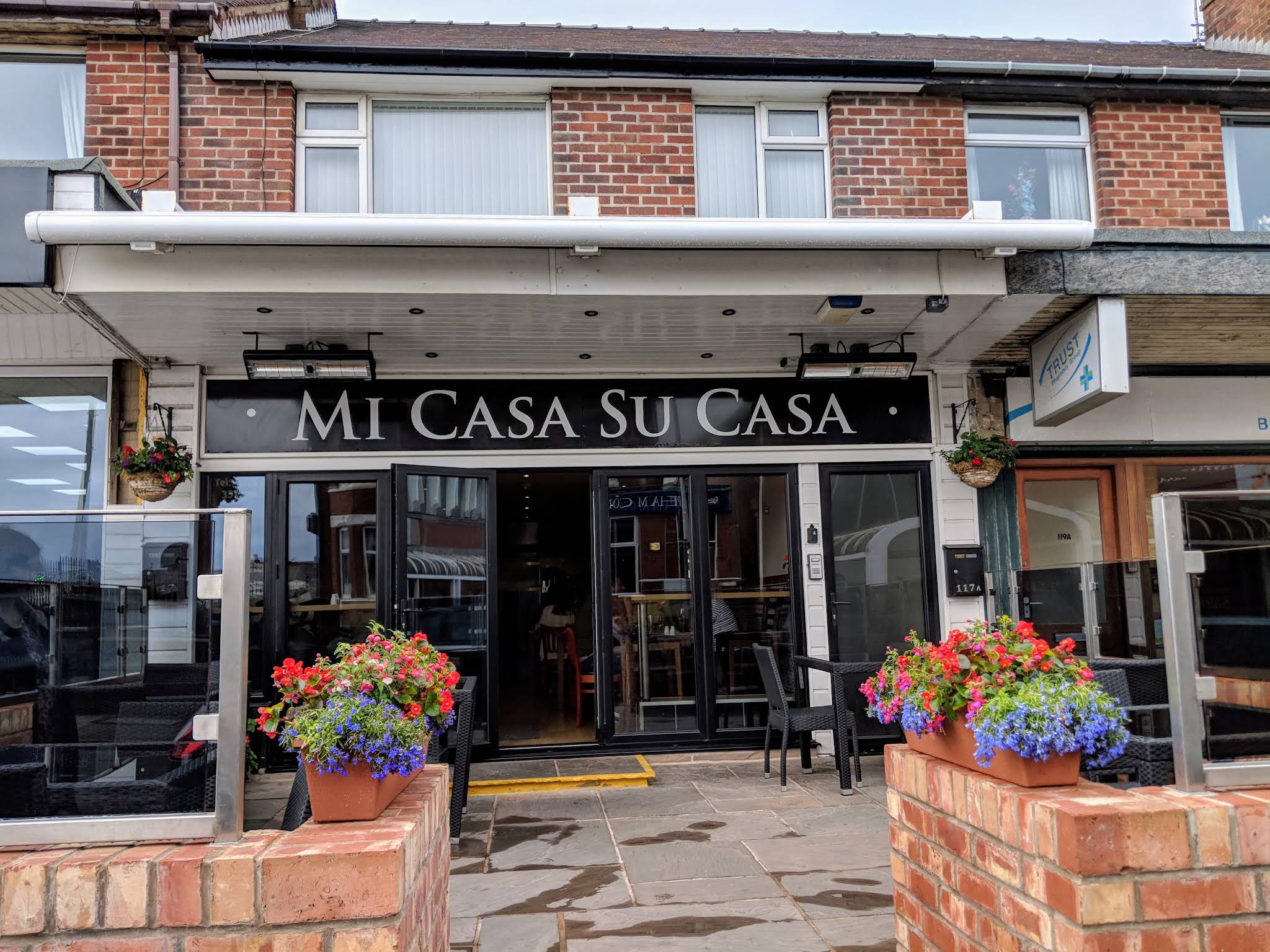 Mi Casa Su Casa's complete entrance, black name sign, flower planters and threshold on Red Bank Road